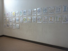 廊下の白い壁にいくつもの動物の絵が等間隔に貼られている写真