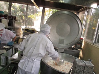 白衣で帽子をかぶった作業員が大きな釜で炊いたご飯を別容器に移している様子