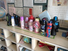 教室後方のロッカーの上に置かれた、複数の児童用の水筒の写真