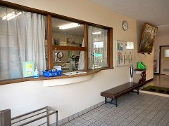 白いカーテンのかけられた窓口にベンチや傘立てが設置されている来訪者用の玄関の写真