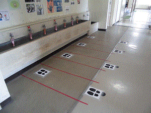 床にテープや足跡のステッカーを貼っている手洗い場の写真