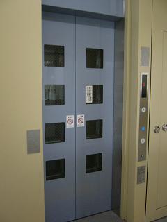 正方形の窓が複数取り付けられた水色のエレベーター扉の写真