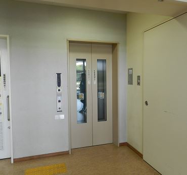 防護壁の隣に設置をされた温かみのある雰囲気のエレベーターの写真