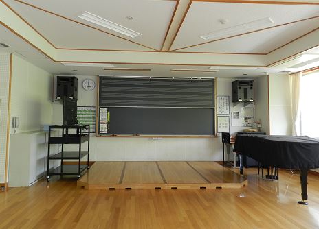 グランドピアノと、中央に合奏用の簡易ステージが用意されている音楽室の写真
